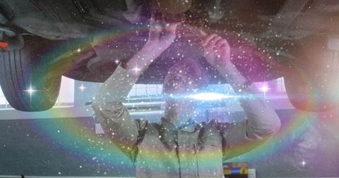 Automotive technician inspecting undercarriage on lift with rainbow light and lens flare