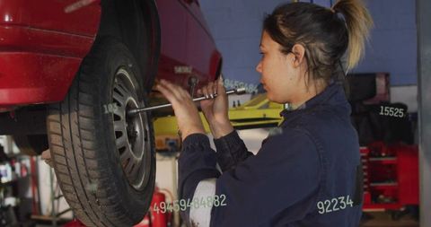 Female mechanic tightening lug nuts on rear wheel while working at garage lift