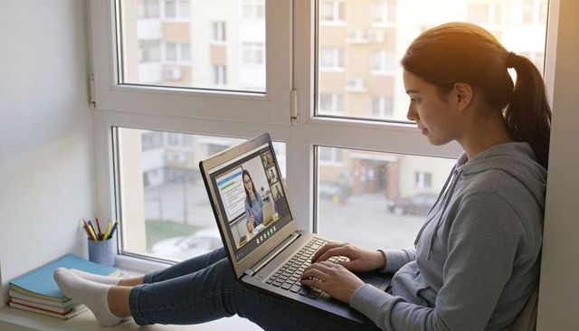 Teen female studying on laptop at window ledge for remote learning and online education