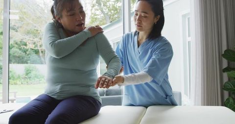 Clinician assisting patient with shoulder mobility assessment and gentle arm stretch at home