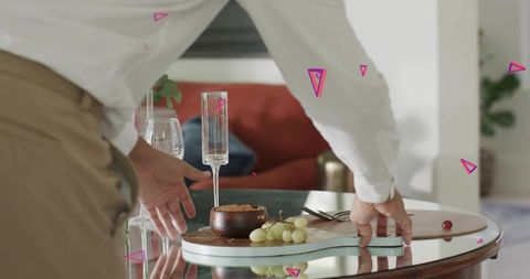 Man arranging elegant snack board with grapes and champagne flute on glass table