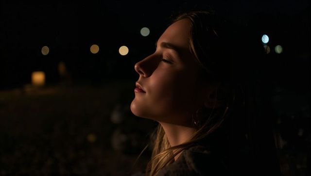 Young woman relaxing at night tilting head back with eyes closed warm lamp bokeh portrait