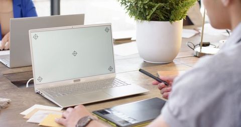Diverse team collaborating around laptop and graphics tablet in modern coworking workspace