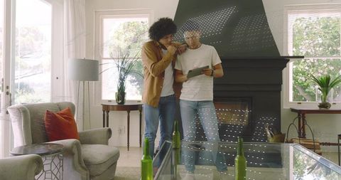 Two men leaning and pointing at tablet in modern living room with fireplace and plants