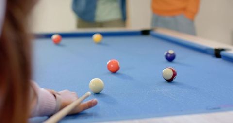 Friends lining up pool shot on blue felt, cue aligning white cue ball, casual billiards
