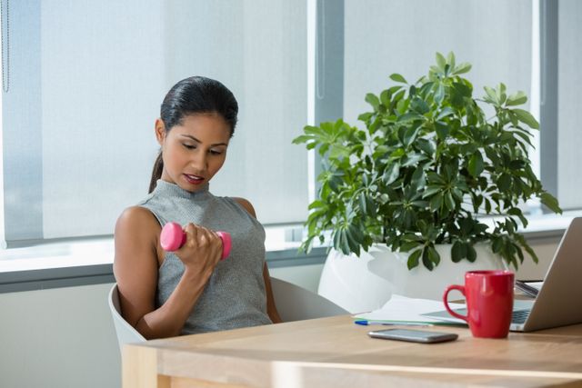 Executive exercising with dumbbells at desk in office