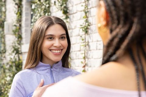Smiling diverse women chatting in sunlit courtyard wearing lavender zip-up, braided hair