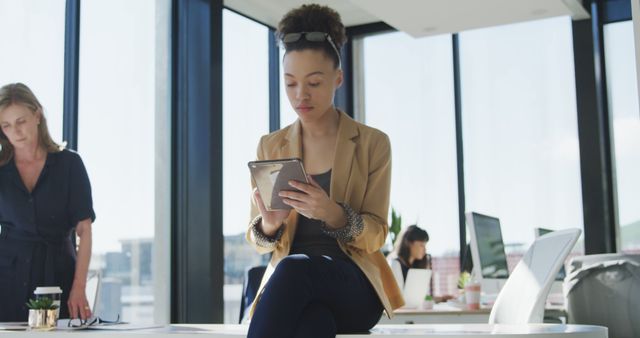 Businesswoman Using Tablet in Modern Office Setting with Colleague in Background - Download Free Stock Images Pikwizard.com