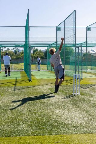 Male cricket players practicing fast bowling in netted training lanes on synthetic turf