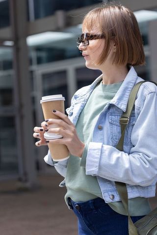 Young woman holding two takeaway coffees while standing outside modern glass building