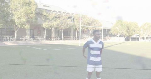 Rugby athlete standing on turf wearing blue white striped jersey looking right in sunlight