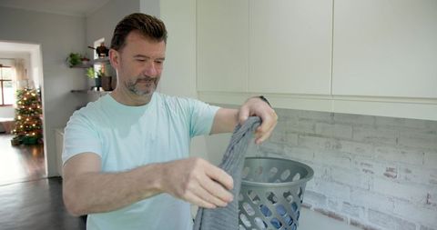 Mature man folding laundry in modern kitchen during christmas time
