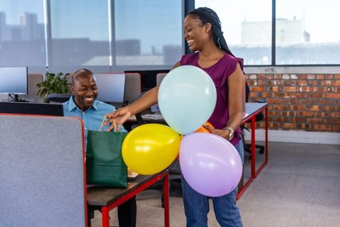 Smiling coworkers exchanging gift bags and balloons in modern office