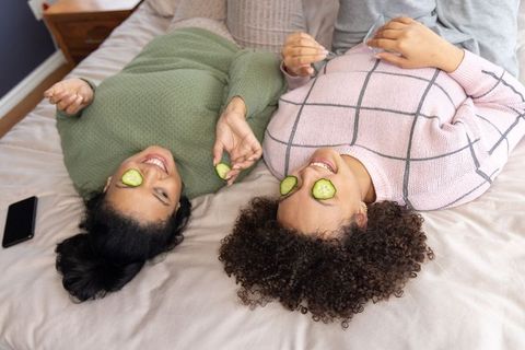 African american and asian friends relaxing with cucumber slices on eyes in cozy sweaters