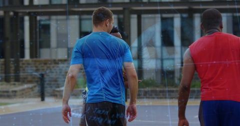 Men walking toward urban streetball court showing camaraderie, fitness, outdoor basketball