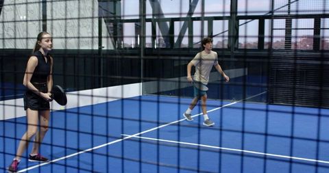 Mixed pair engaging in intense padel match on modern indoor court