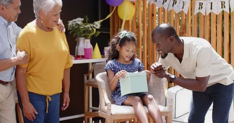 Joyful birthday celebration: young girl and family enjoying gift opening