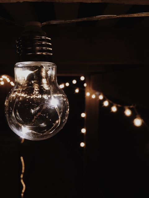 A close-up of a glowing light bulb with additional string lights in the background, creating a warm, inviting ambiance. This image is perfect for showcasing indoor decorations, evoking a sense of coziness, or promoting products related to lighting and home decor.