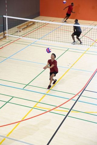 Indoor volleyball team practicing forearm pass on hardwood court with asian teen player