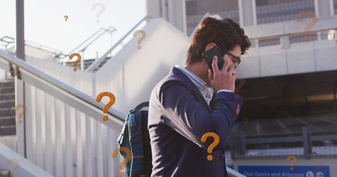 Confused businessman talking on smartphone amid question marks