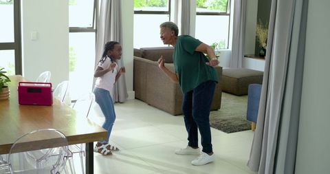 Grandmother and granddaughter dancing joyfully in bright modern living room