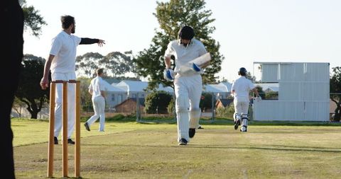 Cricket Players Running Between Wickets on Grass Field