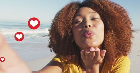 Smiling Woman Blowing Kisses with Heart Icons on Beach