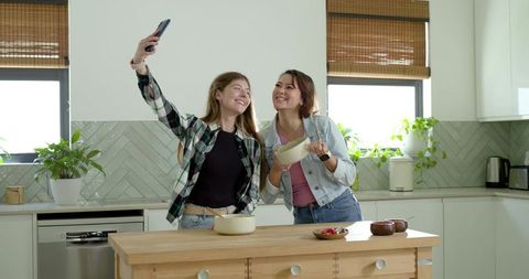 Two friends taking selfie in bright modern kitchen holding bowl and spoon