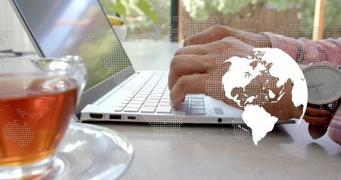 Indian man typing on laptop in bright home workspace with tea cup and digital globe overlay
