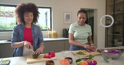 Two friends cooking together chopping fresh veggies on modern kitchen island at home
