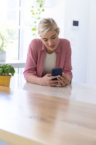 Young woman checking smartphone while leaning on modern kitchen island in natural light