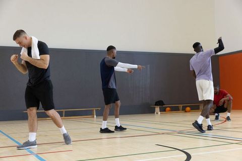 Diverse male teammates warming up and executing basketball drills on indoor hardwood court