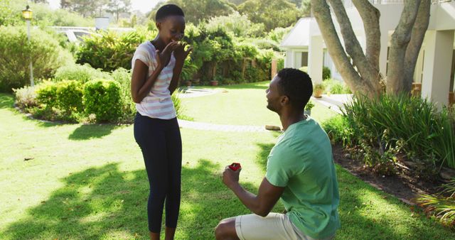 Happy african american couple in sunny garden man kneeling holding ring proposing to woman - Download Free Stock Photos Pikwizard.com