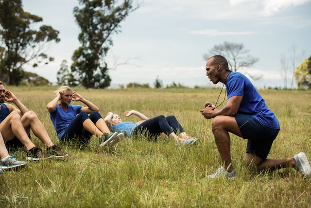 Group of fit individuals performing crunches under the guidance of a fitness instructor in an outdoor bootcamp. Ideal for promoting fitness classes, personal training services, outdoor workout programs, and healthy lifestyle campaigns.