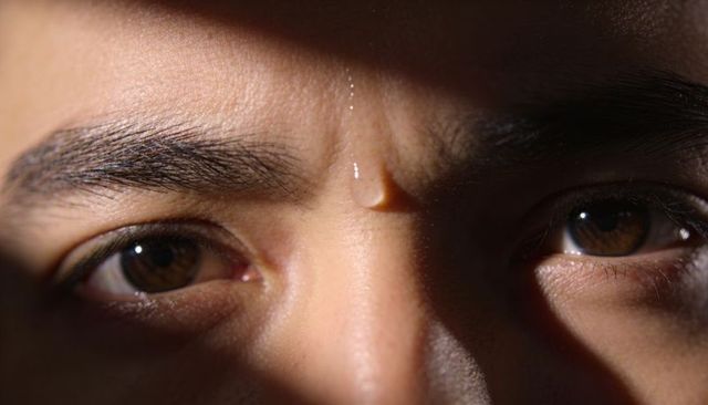 Staring male closeup with water droplet on forehead and brown eyes catching highlights