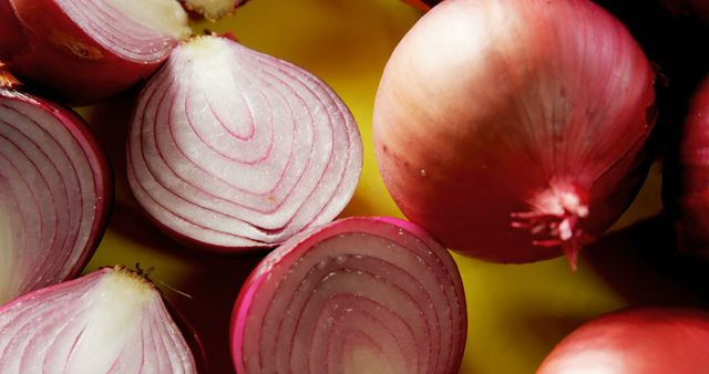 This image showcases fresh red onions, both whole and sliced in halves and quarters, laid out on a yellow background. The vibrant colors and intricate details of the onions make it an ideal choice for use in food blogs, culinary websites, recipe books, and advertisements promoting fresh produce and healthy eating. It can also be used to enhance any material related to cooking, farming, or organic products.