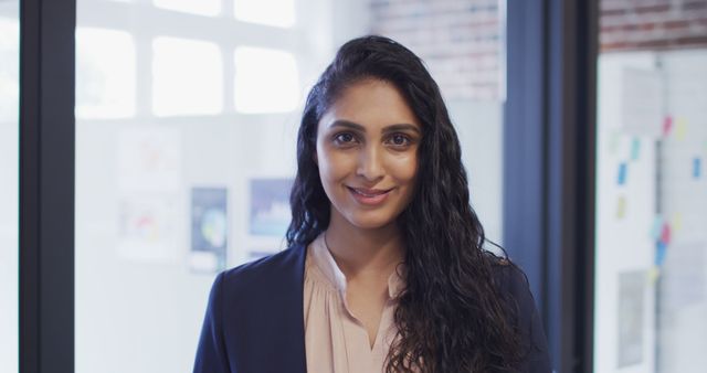 This image depicts a confident Indian businesswoman smiling warmly in a modern office environment. Ideal for use in business-related materials, diversity and inclusion campaigns, corporate websites, and professional presentations. The setting suggests a contemporary workplace with natural light, indicating a positive and collaborative work atmosphere. Perfect for demonstrating leadership, professionalism, and the importance of diversity in the workplace.