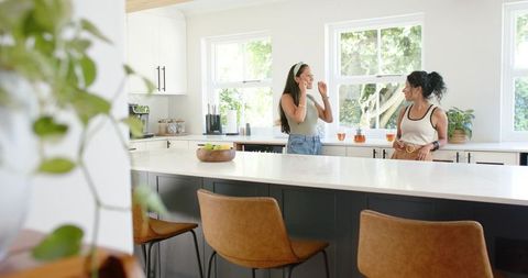 Two friends chatting in bright modern kitchen with marble island and barstools