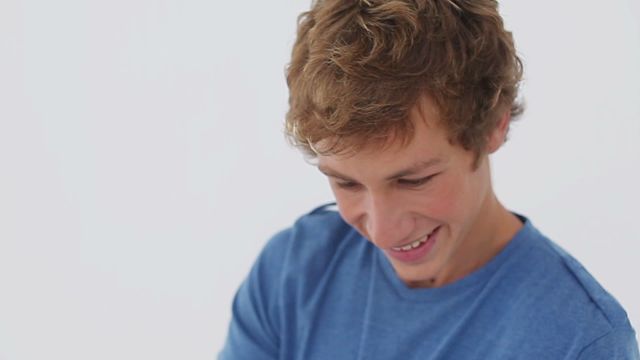 Young man wearing a blue shirt while smiling and taking a selfie against a neutral, white background. Ideal for technology, social media, and lifestyle themes. Can be used in articles or promotions about happiness or using smartphones for selfies.