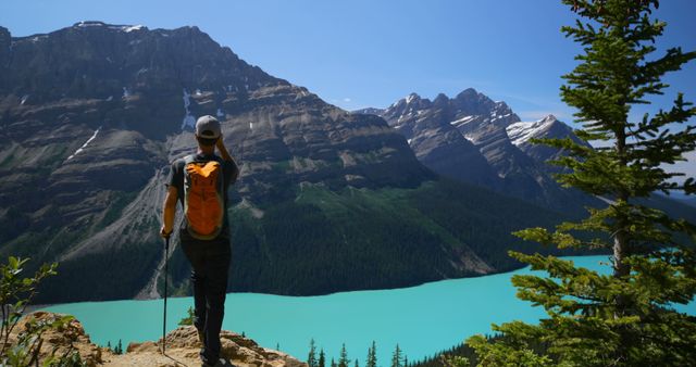 Caucasian male tourist standing on cliff and looking at mountains by sunny lake. Summer, vacations, traveling and active lifestyle, unaltered.