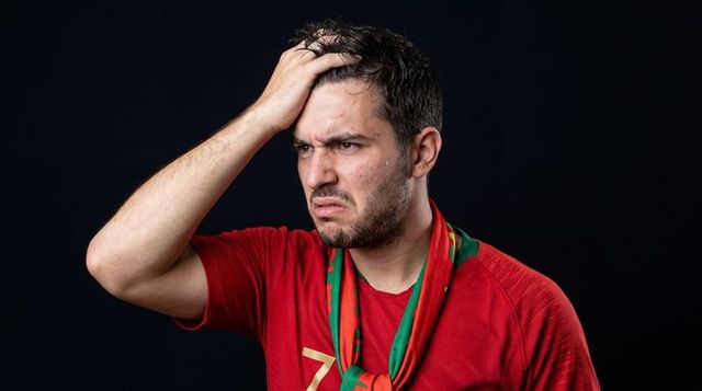 Frustrated soccer fan grabbing head wearing red jersey and national scarf portrait