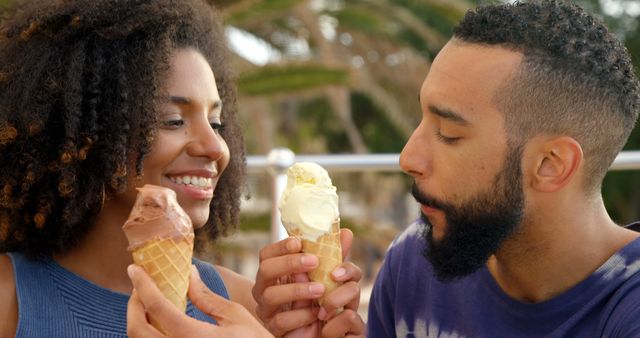 Romantic diverse couple siting by railing, smiling and eating ice creams - Download Free Stock Photos Pikwizard.com