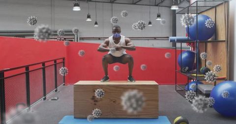 Masked athlete performing plyometric box squat in industrial gym with virus overlay