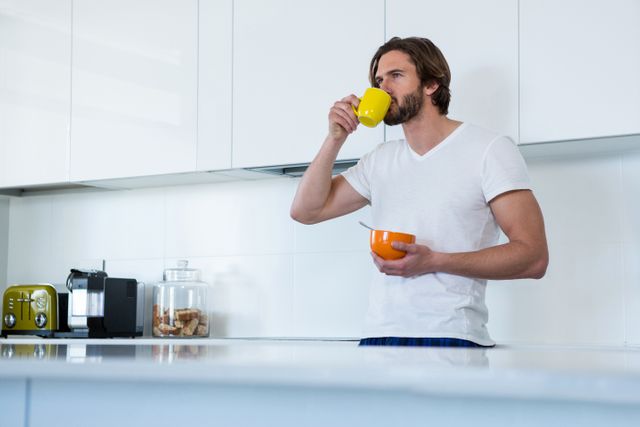 Man drinking coffee while having breakfast in kitchen at home