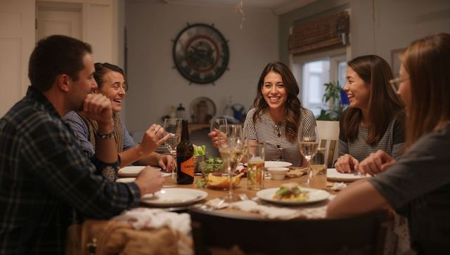 Friends sharing cozy dinner party laughing around home dining table with wine