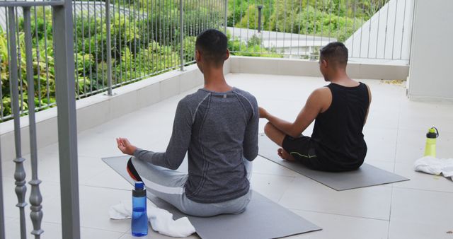 Biracial gay male couple standing on terrace practicing yoga meditating. staying at home in isolation during quarantine lockdown.
