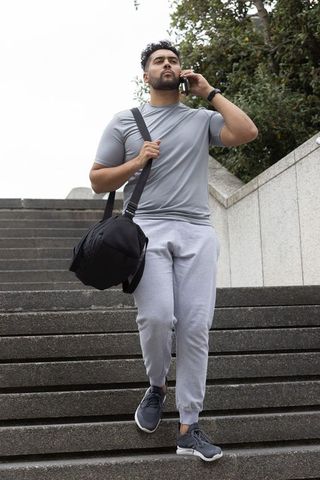 African american man descending concrete stairs calling on phone carrying black duffel