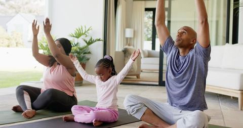 Diverse family practicing yoga at home together stretching with child in sunlit living room