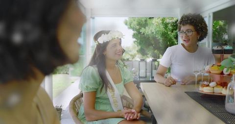 Smiling bride-to-be celebrating bridal shower with friends wearing floral crown and dessert display