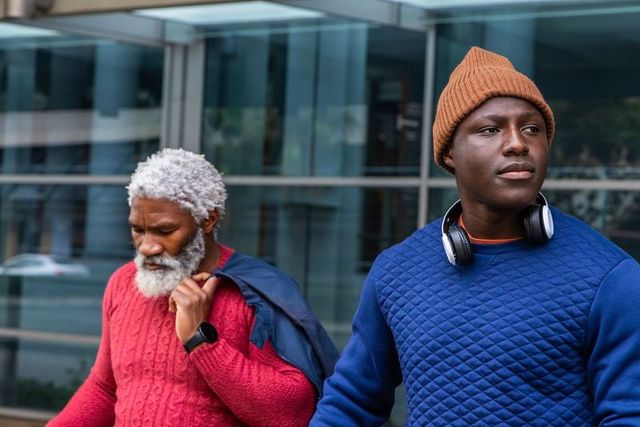 African american senior and man walking on urban sidewalk wearing beanie and headphones